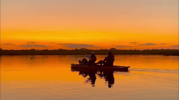 Beautiful Orange sunset with kayakers using pedals on clear calm waters.